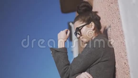 漂亮的时髦女人穿着灰色外套站在城市的街道上布鲁内特女孩近墙手表相机视频的预览图