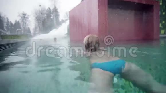 穿着蓝色比基尼的年轻女子在室外游泳池里游泳远离照相机视频的预览图