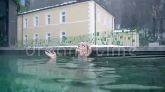 穿着蓝色比基尼的年轻女子向镜头游去陶醉在室外游泳池里视频的预览图