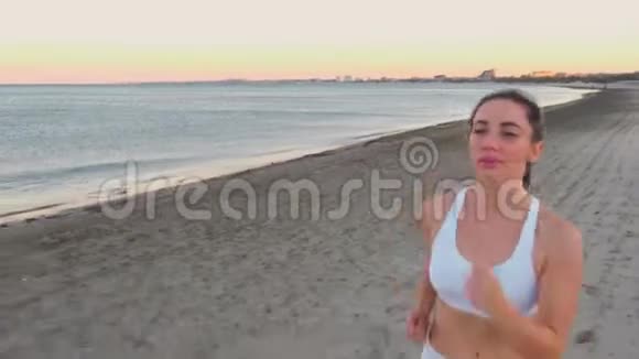 秋天日出时年轻女子正在海边的沙滩上慢跑视频的预览图