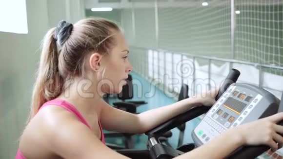 漂亮的女孩在健身房里骑着一辆静止的自行车锻炼视频的预览图
