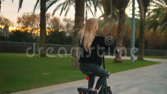 在城市公园驾驶电动自行车的金发美女视频的预览图