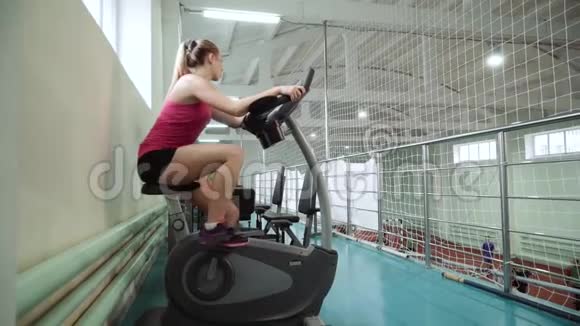 漂亮的女孩在健身房里骑着一辆静止的自行车锻炼视频的预览图