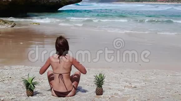 穿着棕色泳衣的女人和菠萝在海滩上在热带巴厘岛享受暑假的年轻女性视频的预览图