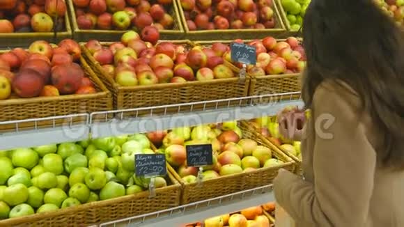 女人在杂货店挑选新鲜的红苹果然后把它放进塑料袋里年轻漂亮的女孩视频的预览图