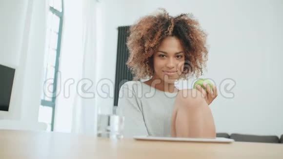 年轻女子坐在家里带着绿苹果对着镜头微笑视频的预览图
