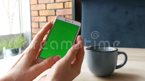 绿色屏幕智能手机白色智能手机上的Chroma键女性的手在一杯咖啡旁边握着手机视频的预览图