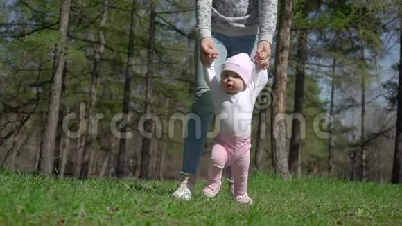 一位年轻的母亲教她的女儿如何走路在公园的绿草上视频的预览图