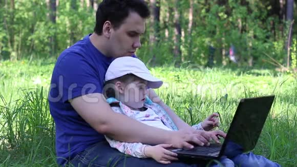 父亲带着女儿坐在草地上手提电脑视频的预览图
