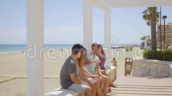 一群朋友坐在靠近海滩的石墙上视频的预览图