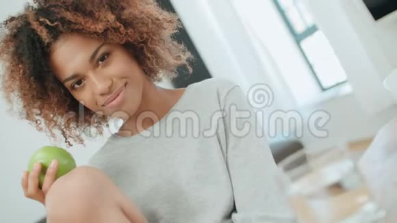年轻女子坐在家里带着绿苹果对着镜头微笑视频的预览图