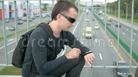 现代年轻人的户外肖像街上有智能手表戴眼镜的人背着背包坐在上面视频的预览图