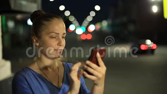 年轻美丽的白种人妇女使用智能手机在城市夜晚手持户外微笑面对视频的预览图