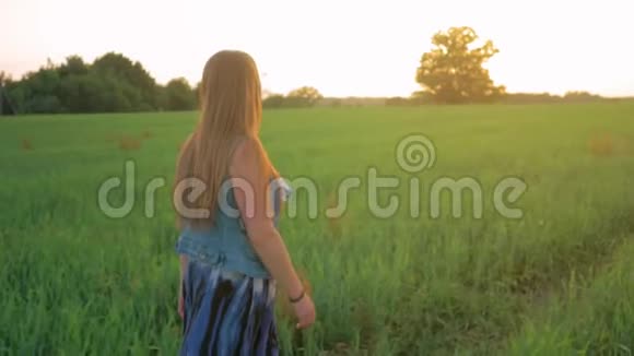 夕阳下一头直发的小女孩走在一片绿色的田野上平均射击慢动作视频的预览图