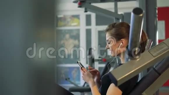 健身房里一个女孩带着手机和耳机的特写镜头视频的预览图