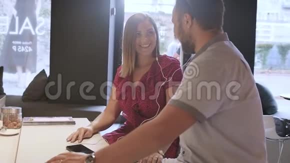 漂亮的年轻夫妇正在咖啡馆里通过耳机听音乐慢动作情侣们喜欢音乐视频的预览图