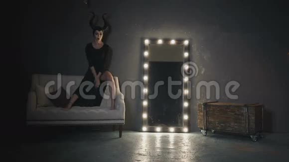 穿着黑色连衣裙长着大角的女孩描绘了坐在白色沙发上的女巫马里芬特视频的预览图