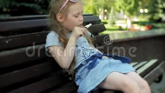 一个小女孩坐在城市的木凳上吃着冰淇淋背景是一个城市公园视频的预览图