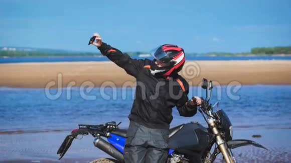 在河岸上的自行车在他的摩托车旁边在电话上拍照视频的预览图