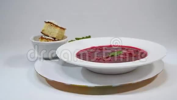 在盘子里用木勺和黑色面包隔离在白色上红甜菜根汤或罗宋汤中的蔬菜和肉类视频的预览图