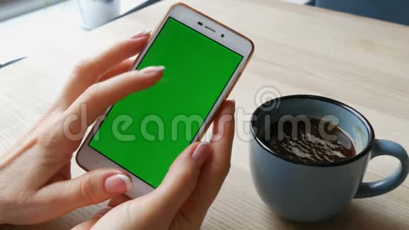 绿色屏幕智能手机白色智能手机上的Chroma键女性的手在一杯咖啡旁边握着手机视频的预览图