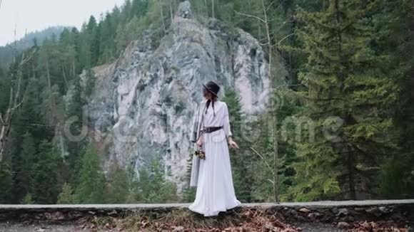 时尚时髦的波霍风格的女人在山区和森林手里拿着花在山里的路上走站起来视频的预览图