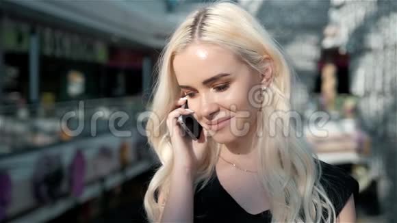 一位年轻貌美的女士使用智能手机站在一家时装店旁边展示着一扇带着假人的玻璃窗视频的预览图