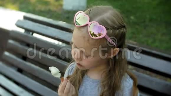 一个小女孩坐在城市的木凳上吃着冰淇淋背景是一个城市公园视频的预览图