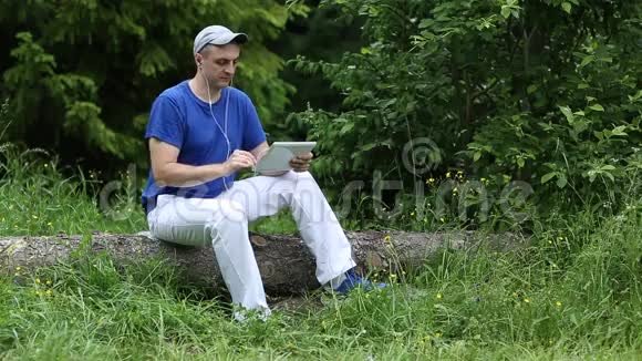 男人坐在原木上拿着小玩意耳机听音乐微笑视频的预览图