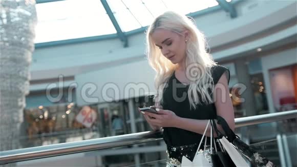 一位年轻貌美的女士使用智能手机站在一家时装店旁边展示着一扇带着假人的玻璃窗视频的预览图