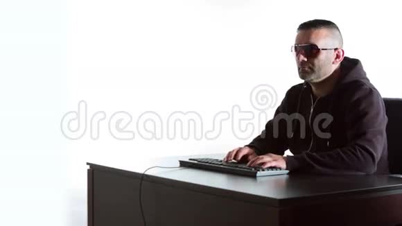 戴墨镜的黑客在电脑键盘上输入白色背景视频的预览图