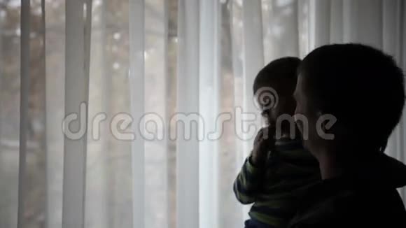 幸福的父亲抱着儿子的手望着窗外的剪影视频的预览图