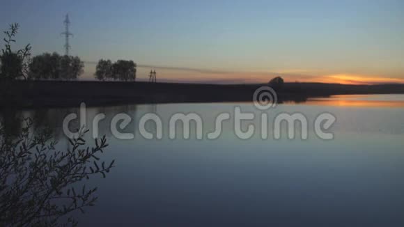 夏日橘色夕阳西下湖岸旁草甸和线路电传输视频的预览图