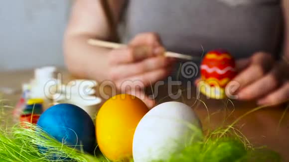 一个年轻的女人在木桌的背景上用刷子抹复活节彩蛋视频的预览图