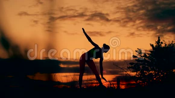 在令人惊叹的日落中女人站在瑜伽姿势的剪影视频的预览图