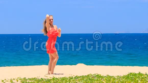 穿红色舞蹈的金发女孩光着脚在沙滩上光滑的头发视频的预览图