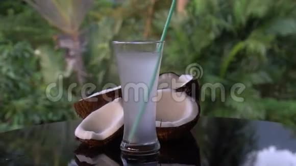 黑色玻璃桌上的椰子和椰子水在模糊的棕榈树背景上被隔离视频的预览图