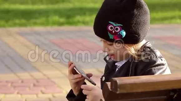 一个女孩在晴天坐在长凳上用手机在公园里的肖像视频的预览图