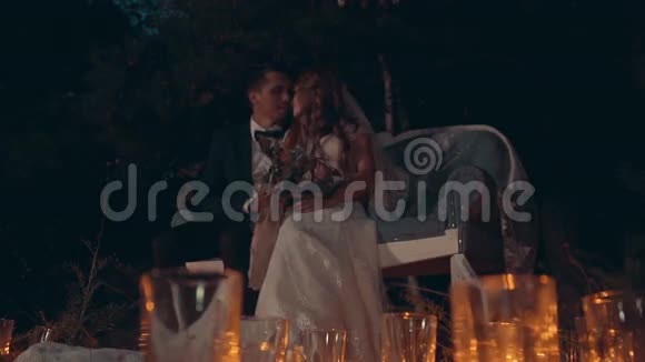 新婚夫妇在夜晚拥抱和亲吻坐在黑暗的森林里的沙发上视频的预览图