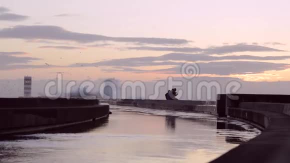 年轻夫妇在有灯塔的防波堤码头享受日落视频的预览图