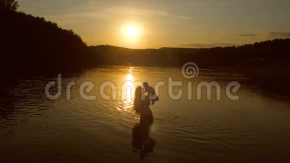 宝宝在妈妈的怀里在夕阳下的水里慢动作视频的预览图