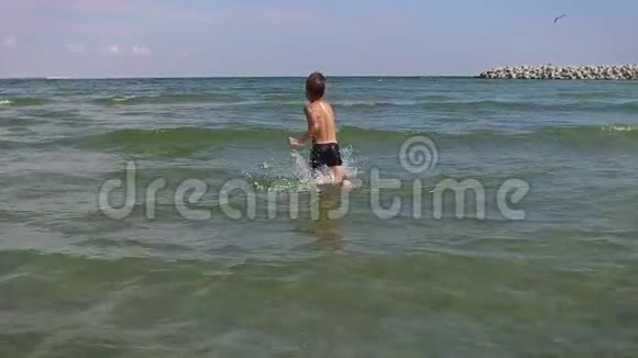 快乐的小男孩跑进水里慢动作视频的预览图