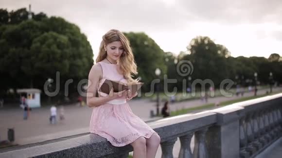 女孩坐在公园的岩石上读着一本书微笑着读着视频的预览图
