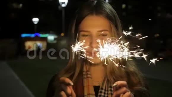 年轻美丽快乐的微笑女孩拿着火花在街上摆姿势街上有火花的女人假日视频的预览图