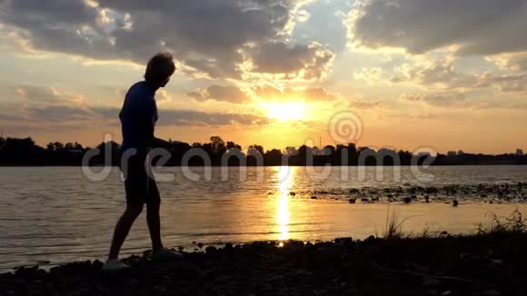在日落时金发人站在河岸上他扔石头视频的预览图
