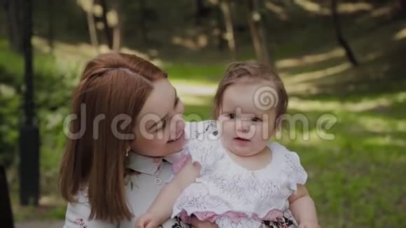 美丽快乐的年轻母亲把女儿抱在公园里视频的预览图