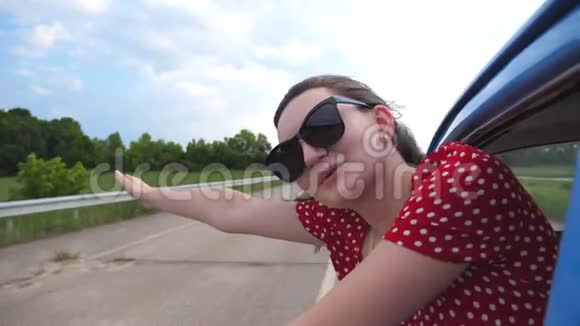 戴着太阳镜的快乐女孩斜靠在老式车窗外享受旅行年轻女子望着窗外移动视频的预览图
