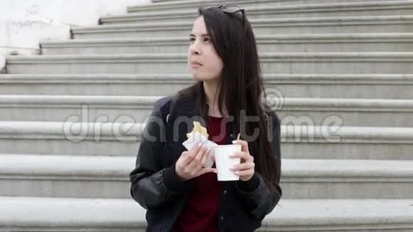 城市里年轻的黑发女人吃三明治喝酒视频的预览图