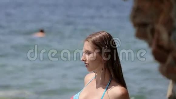 一位留着长发和比基尼的年轻女士站在岩石海滩上摆姿势视频的预览图