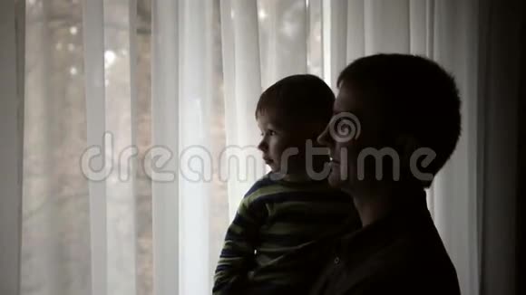 幸福的父亲抱着儿子的手望着窗外的剪影视频的预览图